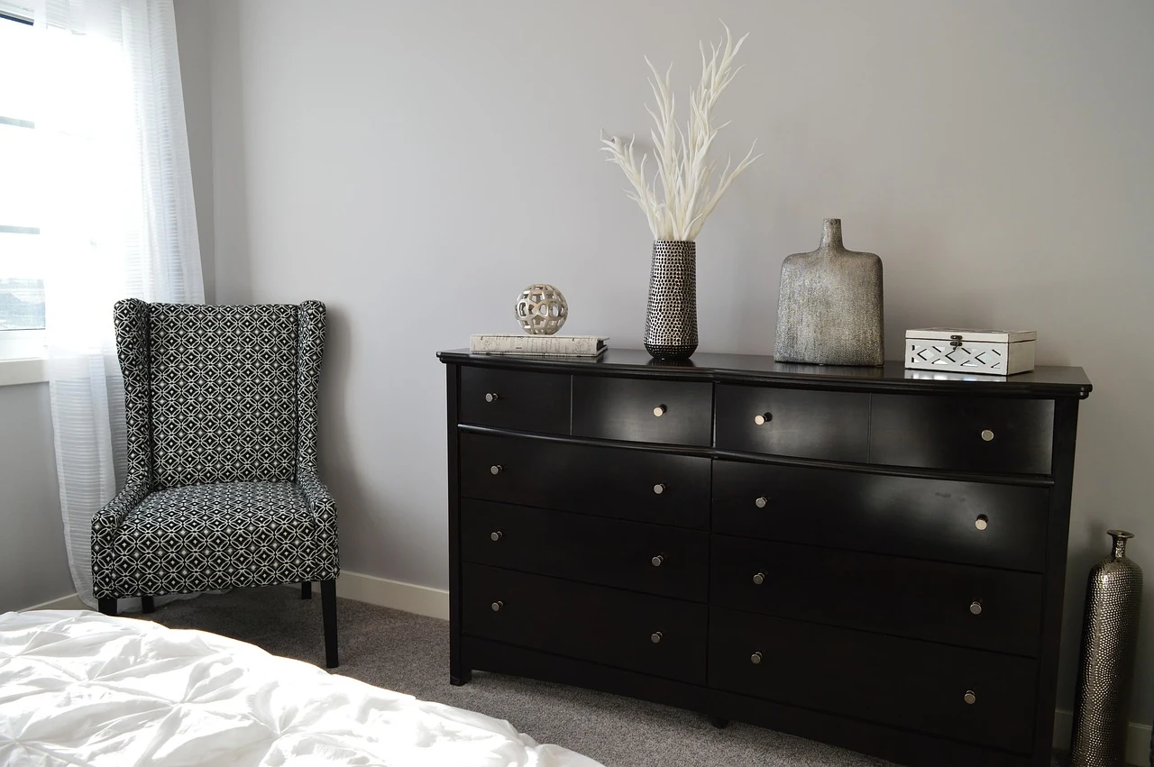 Patterned upholstered chair beside a dark dresser in a pale room