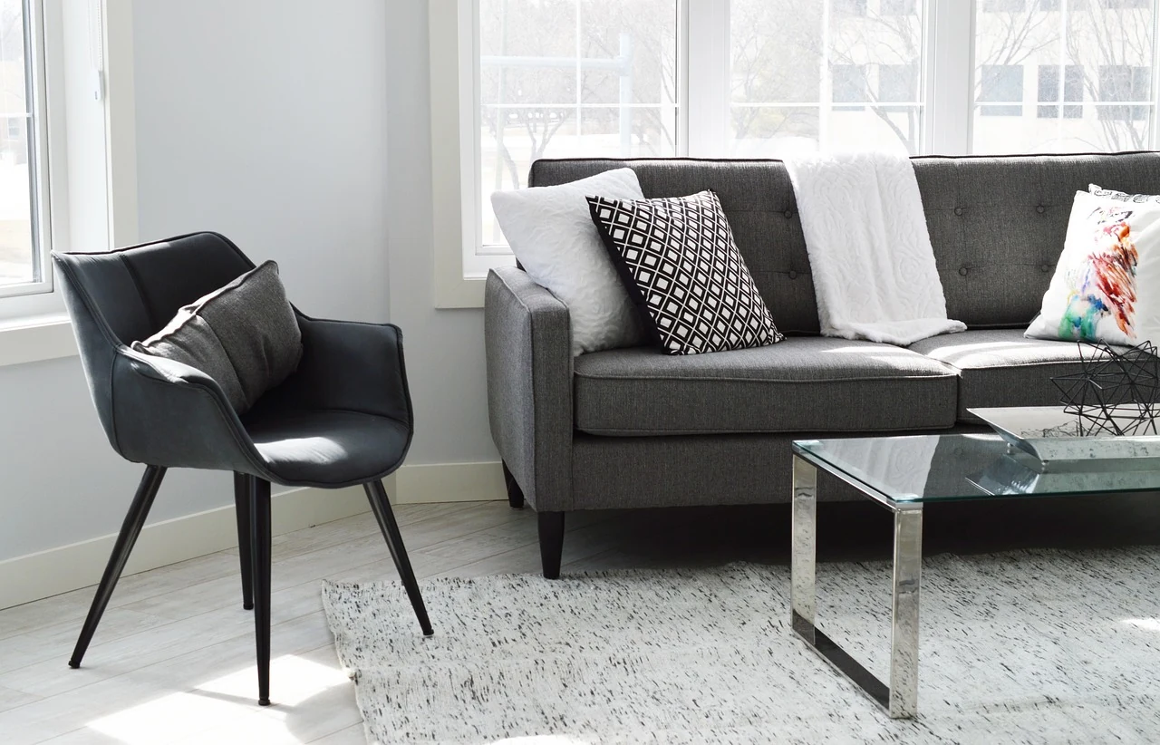 Dark upholstered chair beside a grey sofa and a glass table in a bright room